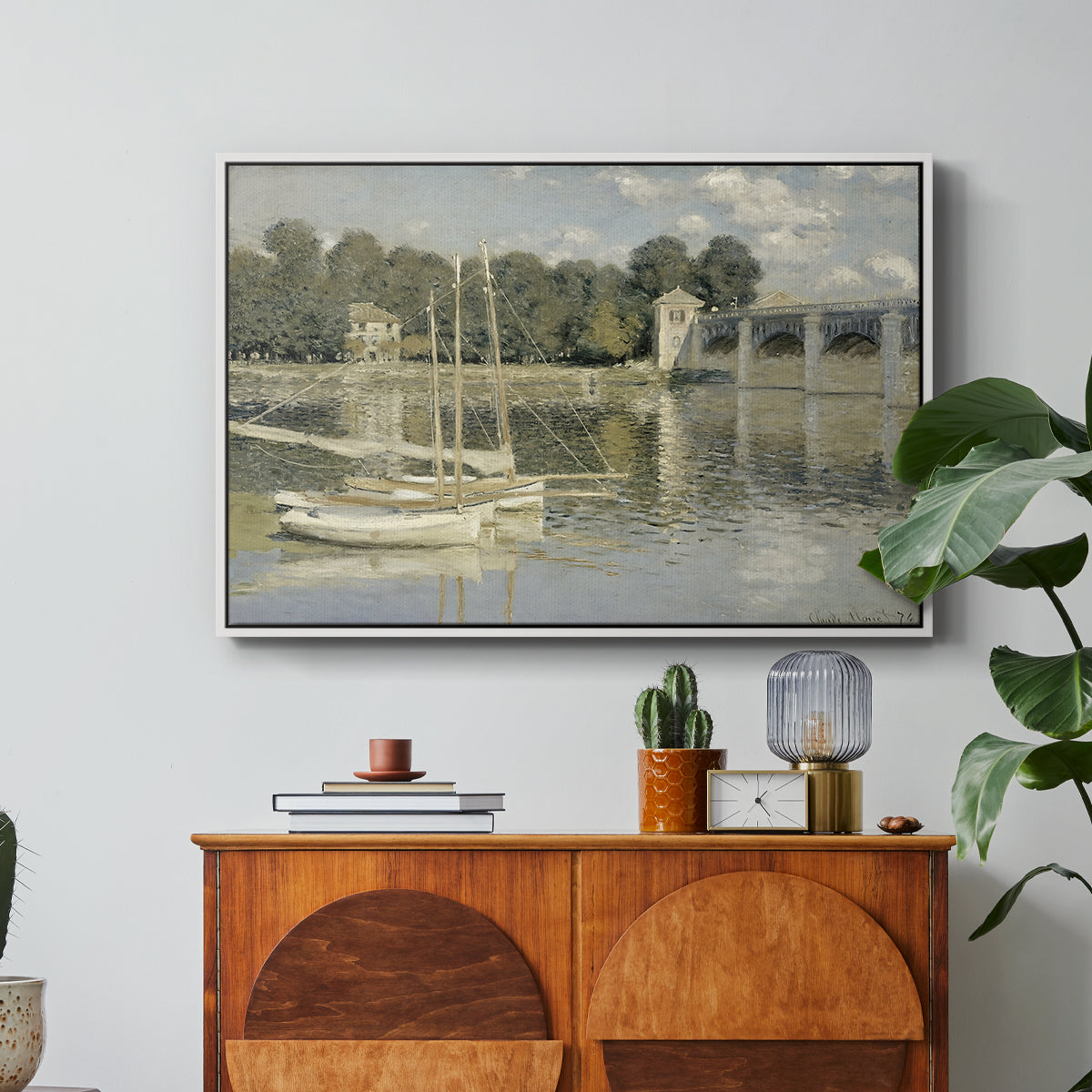 The Bridge at Argenteuil, 1874 by Claude Monet in a white floater framed canvas featuring a bridge spanning river with sailboats and reflections in water, displayed above a wood console cabinet.