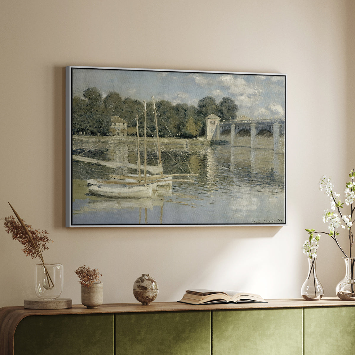 White floater framed canvas of The Bridge at Argenteuil, 1874 by Claude Monet, featuring an impressionist river scene with boats passing beneath bridge above a sideboard in a softly lit hallway.