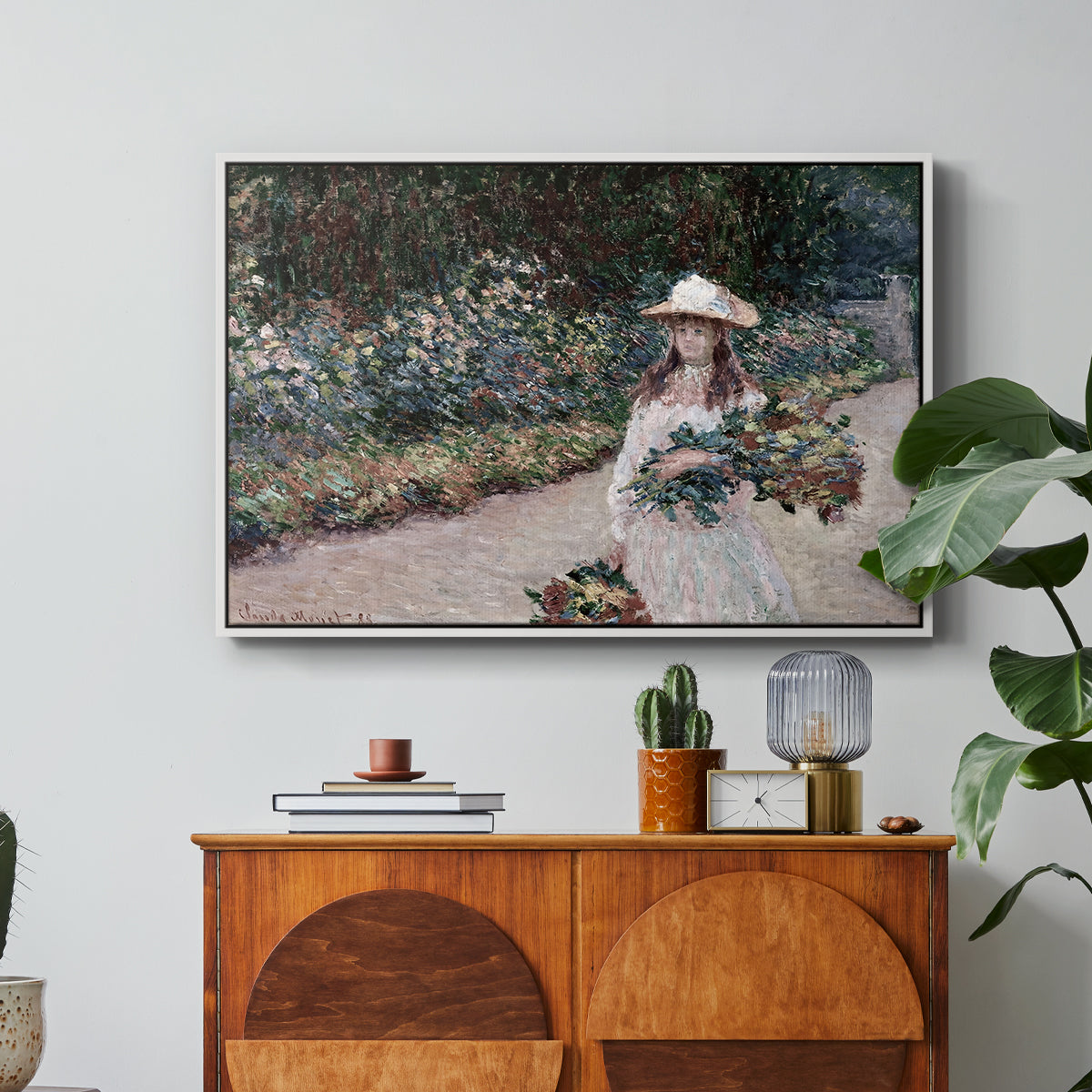 Young Girl in the Garden at Giverny, 1888 by Claude Monet in a white floater framed canvas featuring a young girl seated in lush garden surrounded by blooming flowers, displayed above a wood console cabinet.