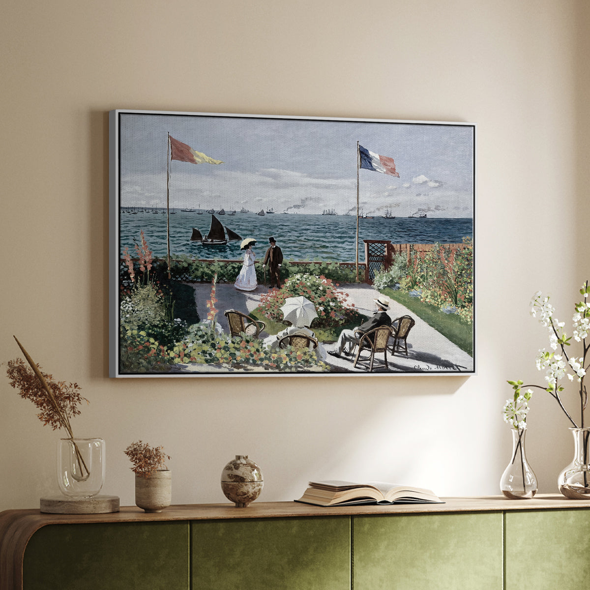 White floater framed canvas of Garden at Sainte-Adresse, 1867 by Claude Monet, featuring an impressionist coastal garden with people and ocean view above a sideboard in a softly lit hallway.
