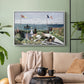 White floater framed canvas featuring a landscaped terrace with figures and flags near shoreline, displayed above a sofa in a modern living room.