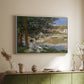 White floater framed canvas of On the Bank of the Seine, Bennecourt, 1868 by Claude Monet, featuring a peaceful riverside scene with figures resting in grassy area by water above a sideboard in a softly lit hallway.