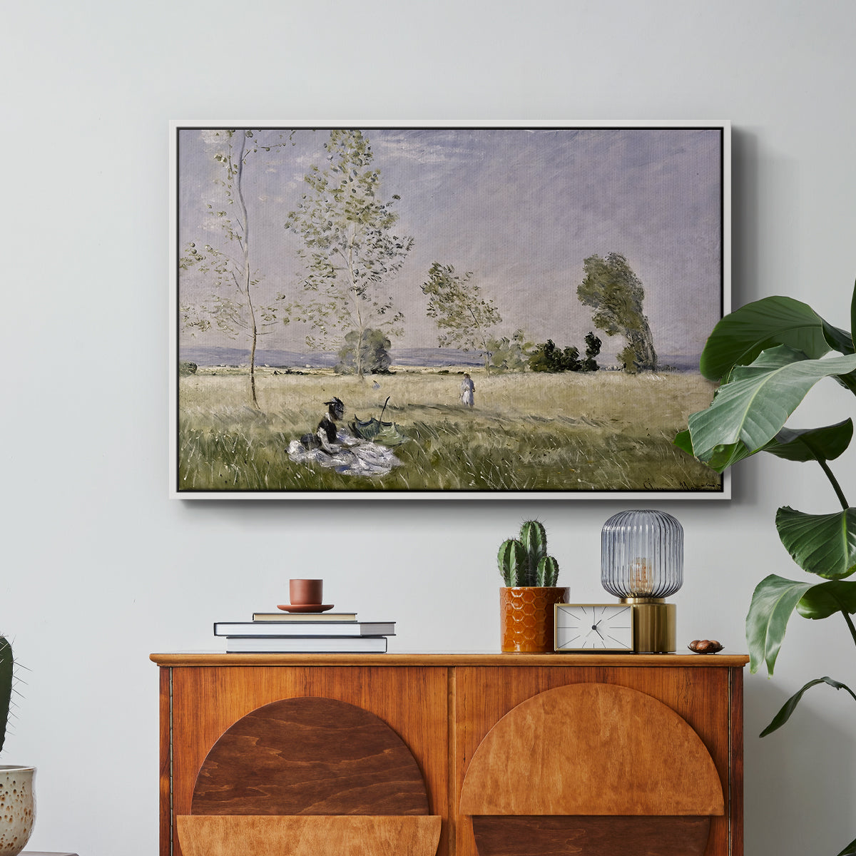 Summer (L'ete), 1874 by Claude Monet in a white floater framed canvas featuring a woman seated in grassy field beneath tree in bright summer landscape, displayed above a wood console cabinet.