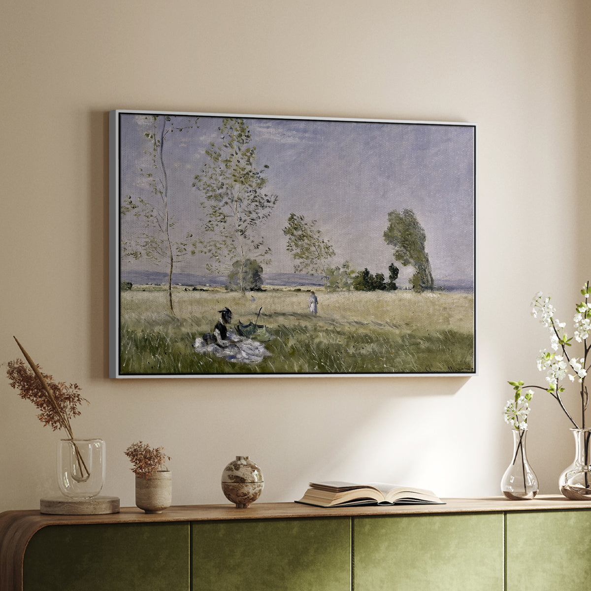 White floater framed canvas of Summer (L'ete), 1874 by Claude Monet, featuring an impressionist countryside scene with figure resting in shade above a sideboard in a softly lit hallway.