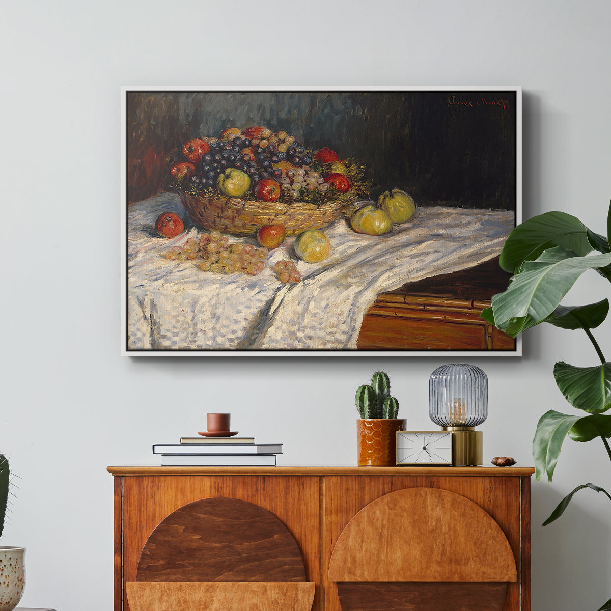 Still Life with Apples and Grapes, 1880 by Claude Monet in a white floater framed canvas featuring an arrangement of apples and grapes on table with soft natural light, displayed above a wood console cabinet.