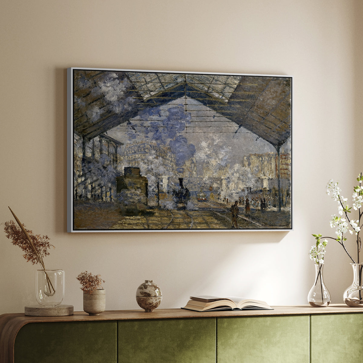 White floater framed canvas of The Gare Saint-Lazare, 1877 by Claude Monet, featuring an impressionist scene of trains and smoke inside busy railway station above a sideboard in a softly lit hallway.
