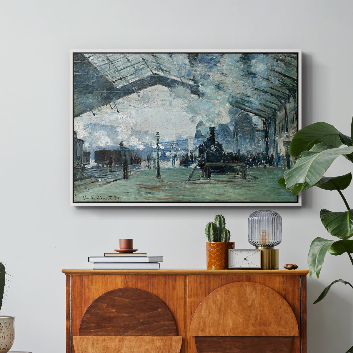 The Saint-Lazare Station, 1877 by Claude Monet in a white floater framed canvas featuring trains arriving under large arched station roof with billowing steam, displayed above a wood console cabinet.
