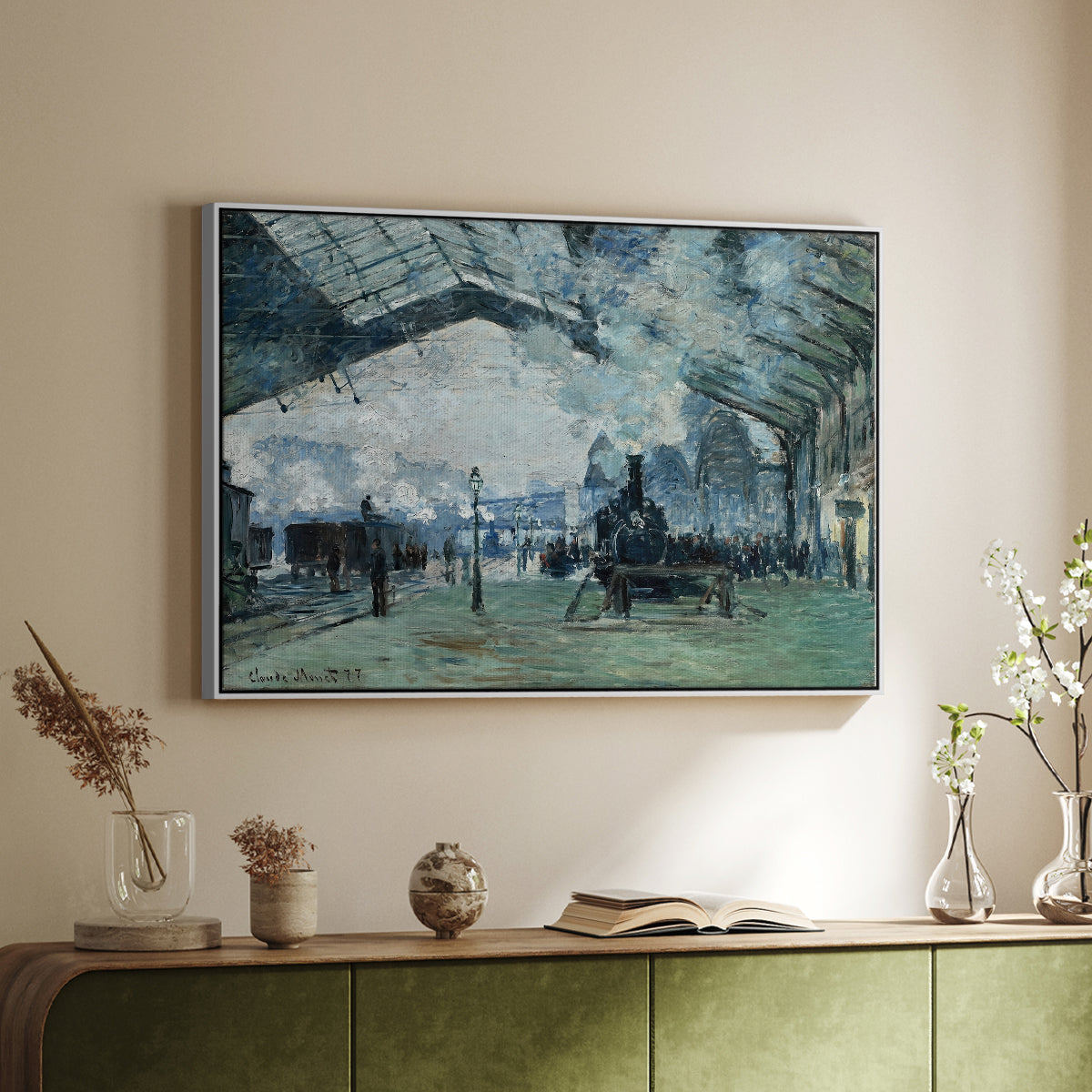 White floater framed canvas of The Saint-Lazare Station, 1877 by Claude Monet, featuring an impressionist railway scene with locomotives and haze above a sideboard in a softly lit hallway.