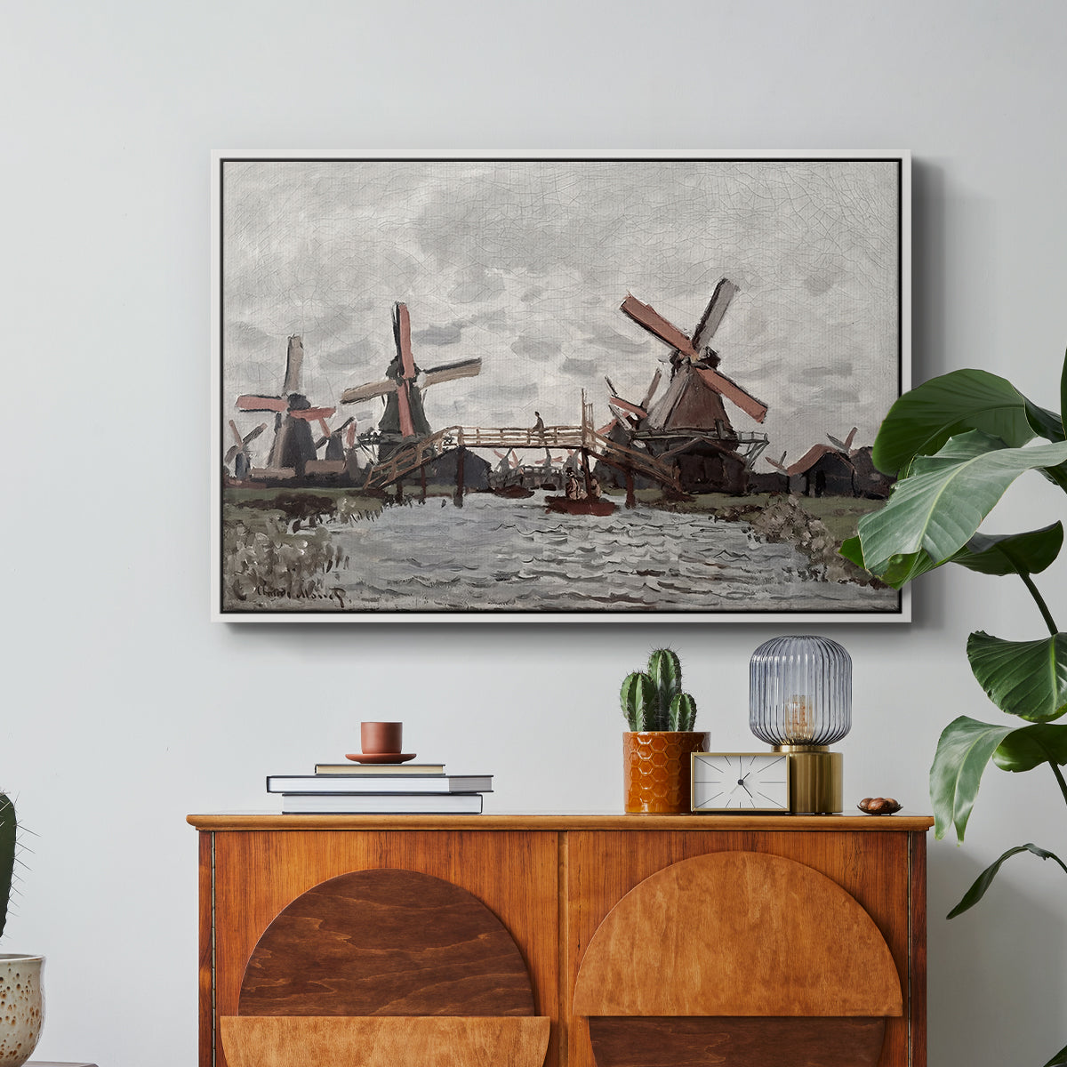 Windmills near Zaandam, 1871 by Claude Monet in a white floater framed canvas featuring windmills standing beside water under open sky in rural landscape, displayed above a wood console cabinet.