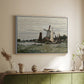 White floater framed canvas of Windmill at Zaandam, 1871 by Claude Monet, featuring an impressionist depiction of windmill near riverbank above a sideboard in a softly lit hallway.