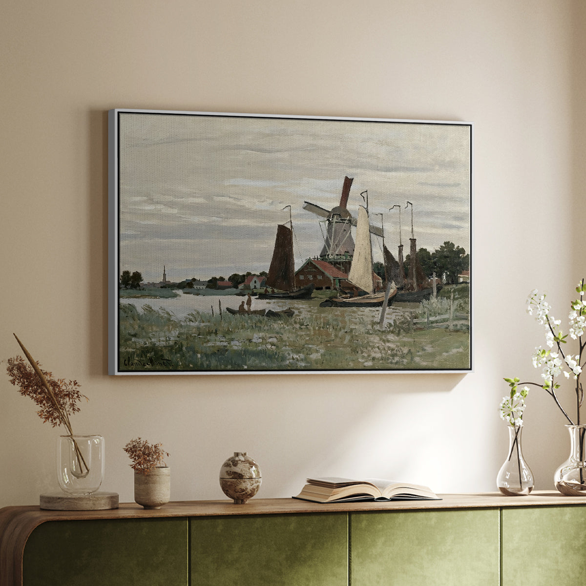 White floater framed canvas of Windmill at Zaandam, 1871 by Claude Monet, featuring an impressionist depiction of windmill near riverbank above a sideboard in a softly lit hallway.