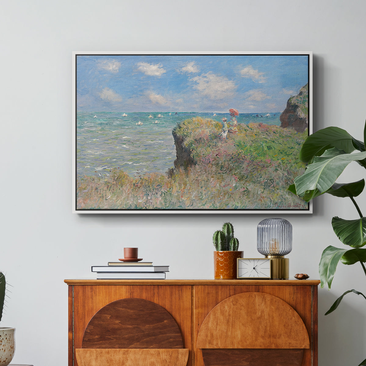 The Cliff Walk at Pourville, 1882 by Claude Monet in a white floater framed canvas featuring figures walking along coastal cliff path overlooking ocean and sky, displayed above a wood console cabinet.
