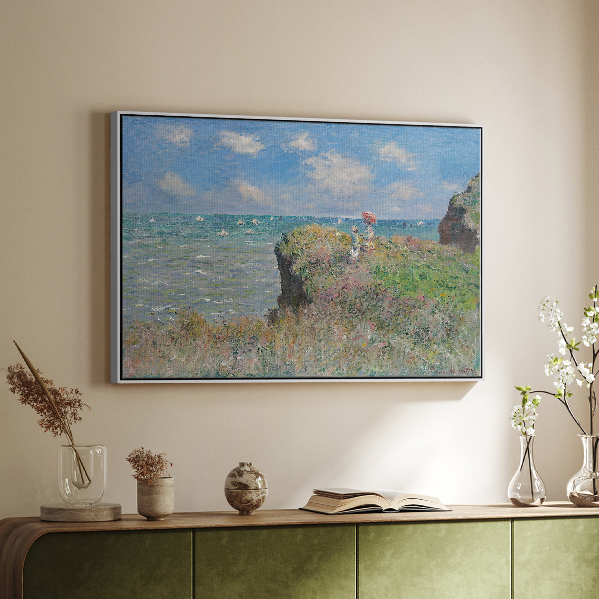 White floater framed canvas of The Cliff Walk at Pourville, 1882 by Claude Monet, featuring an impressionist seaside landscape with people strolling above water above a sideboard in a softly lit hallway.