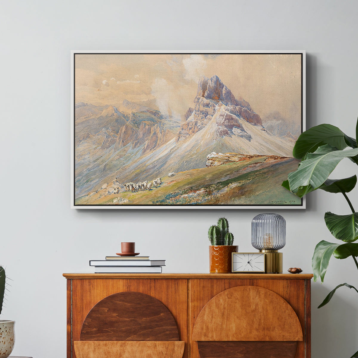 From the Dolomites, 1904 by Edward Theodore Compton in a white floater framed canvas featuring dramatic Dolomite mountain peaks rising above rugged terrain, displayed above a wood console cabinet.