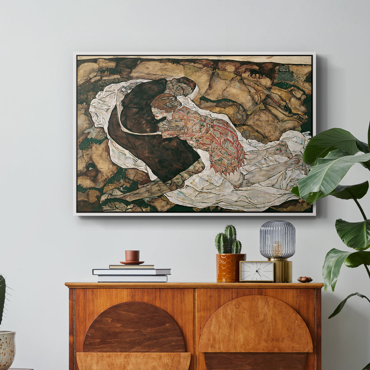 Death and the Maiden, 1915 by Egon Schiele in a white floater framed canvas featuring intertwined figures representing death and woman in emotional embrace, displayed above a wood console cabinet.