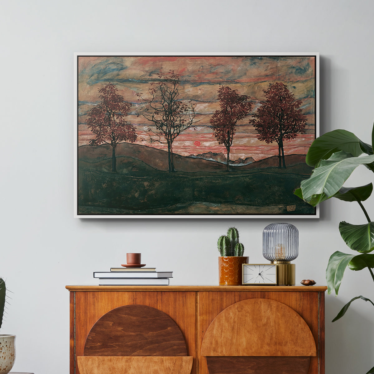 Four Trees, 1917 by Egon Schiele in a white floater framed canvas featuring four trees standing in open landscape against colorful sky, displayed above a wood console cabinet.