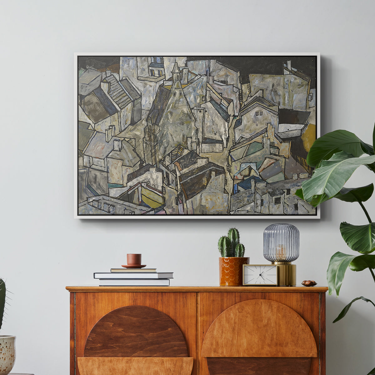 Mödling II, 1918 by Egon Schiele in a white floater framed canvas featuring clustered geometric houses forming dense urban landscape with sharp angles, displayed above a wood console cabinet.