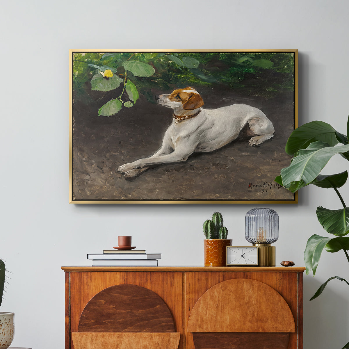 Portrait of a Dog, 1891 by Bruno Liljefors in a gold floater framed canvas featuring a dog lying on ground with head raised in natural outdoor setting, displayed above a wood console cabinet.