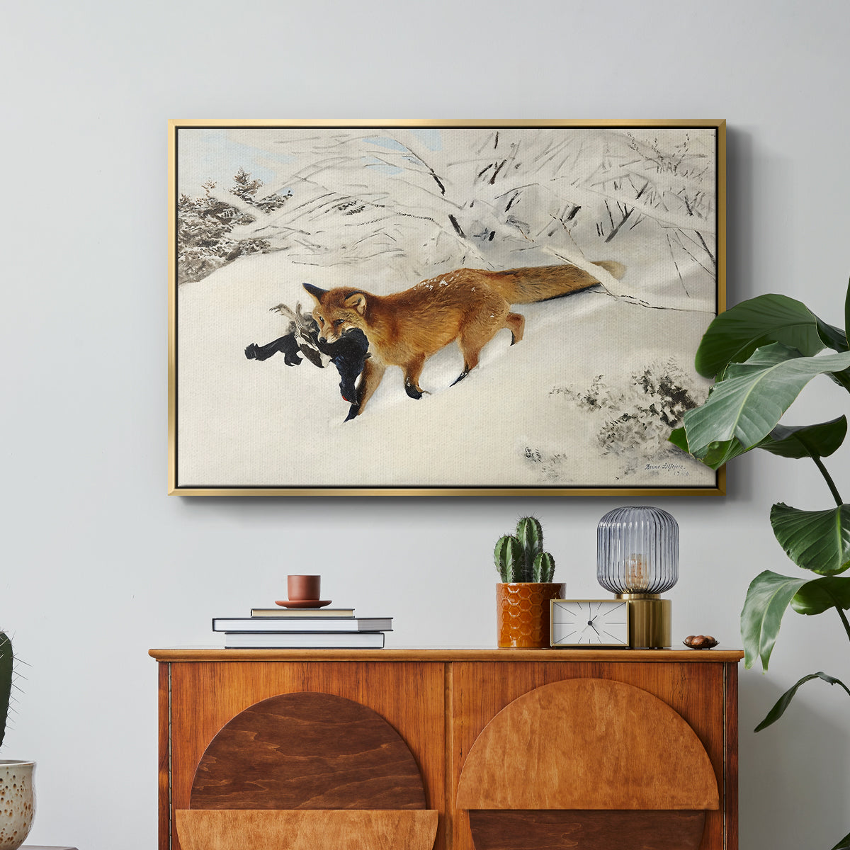 Fox in Snow Landscape, 1900 by Bruno Liljefors in a gold floater framed canvas featuring a fox running across snowy landscape with sparse vegetation, displayed above a wood console cabinet.