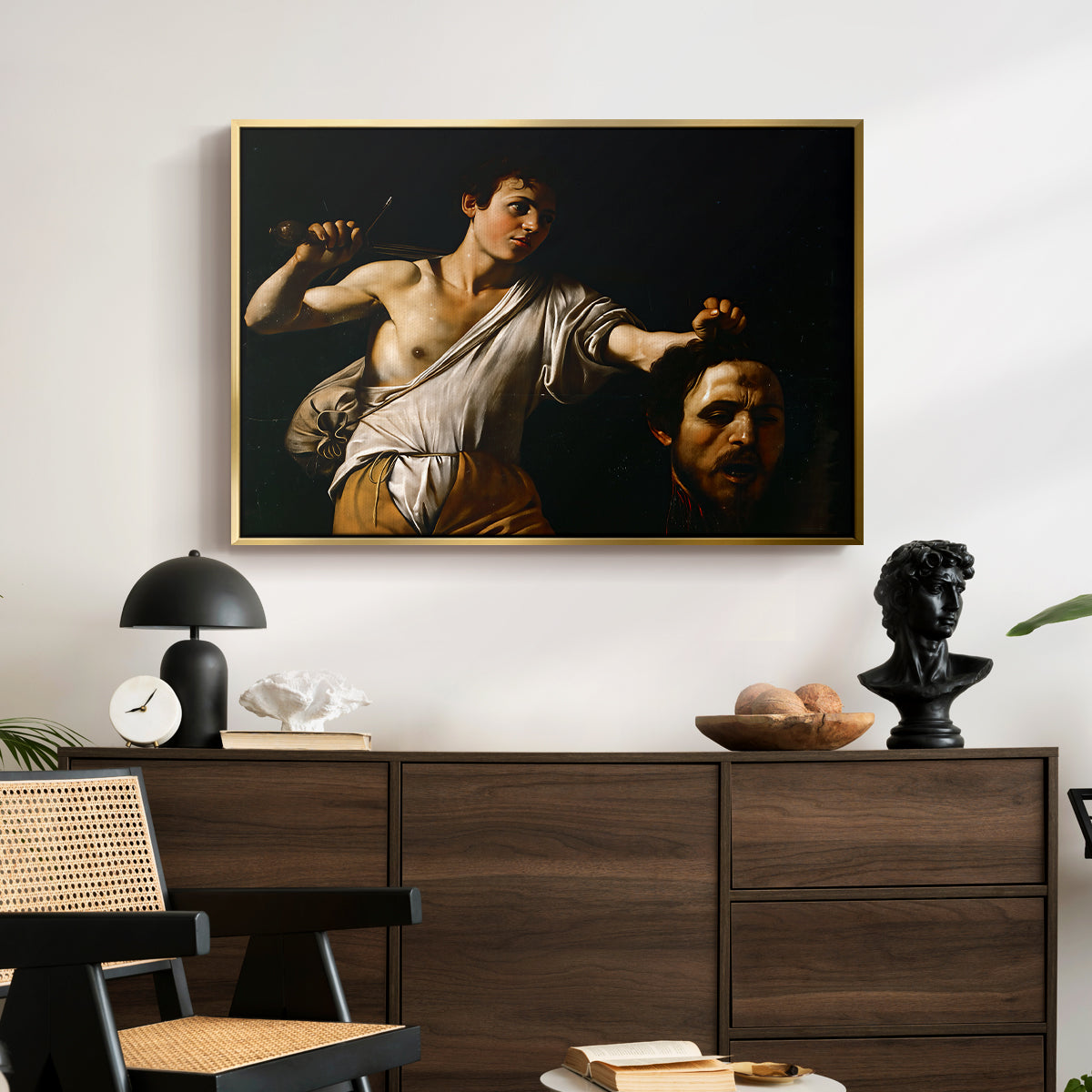 David with the Head of Goliath (Vienna Version), c. 1607 by Caravaggio displayed in a gold floater framed canvas above a dark wood credenza in an entryway.
