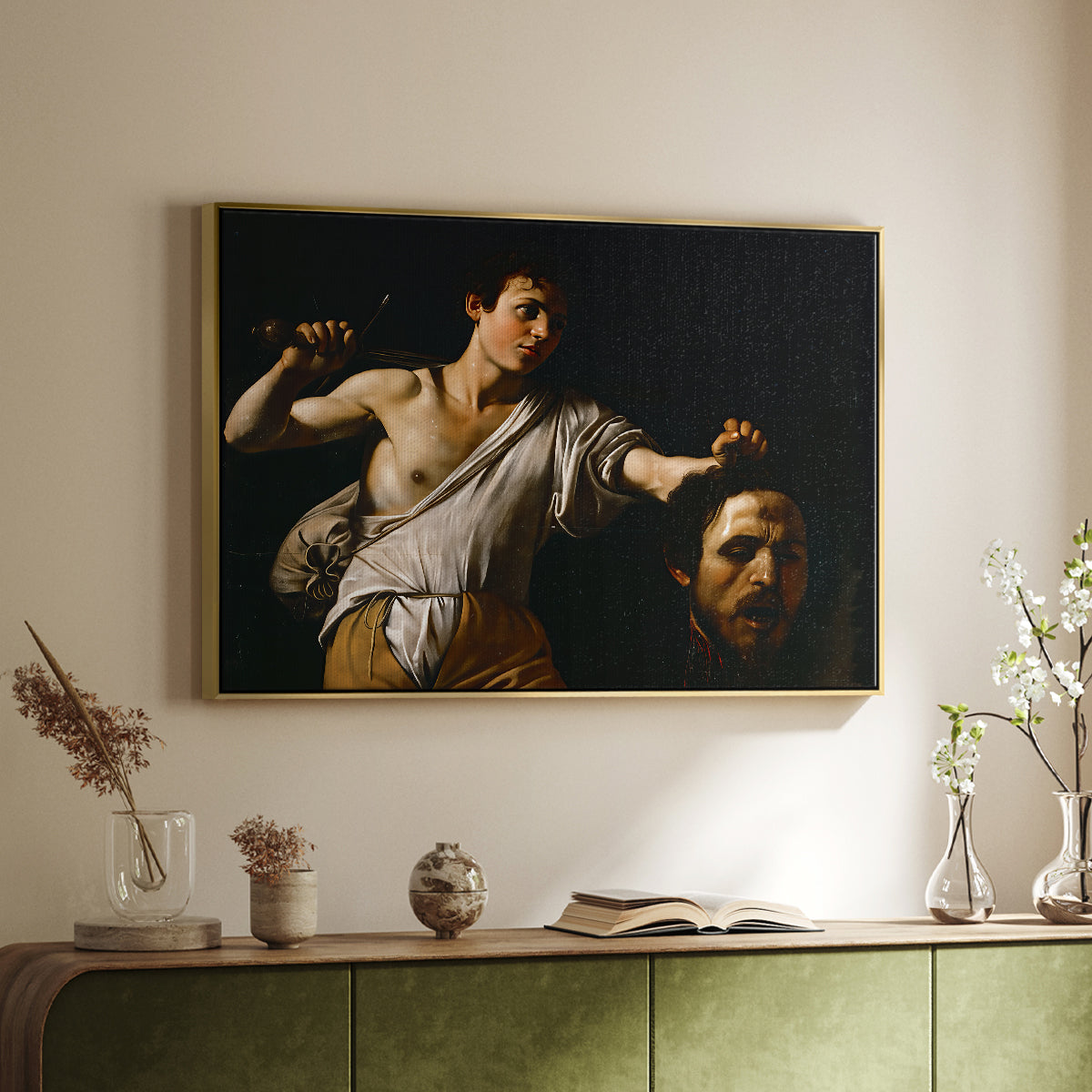 Gold floater framed canvas of David with the Head of Goliath (Vienna Version), c. 1607 by Caravaggio, featuring a biblical scene of David gripping Goliath's head with dramatic lighting above a sideboard in a softly lit hallway.