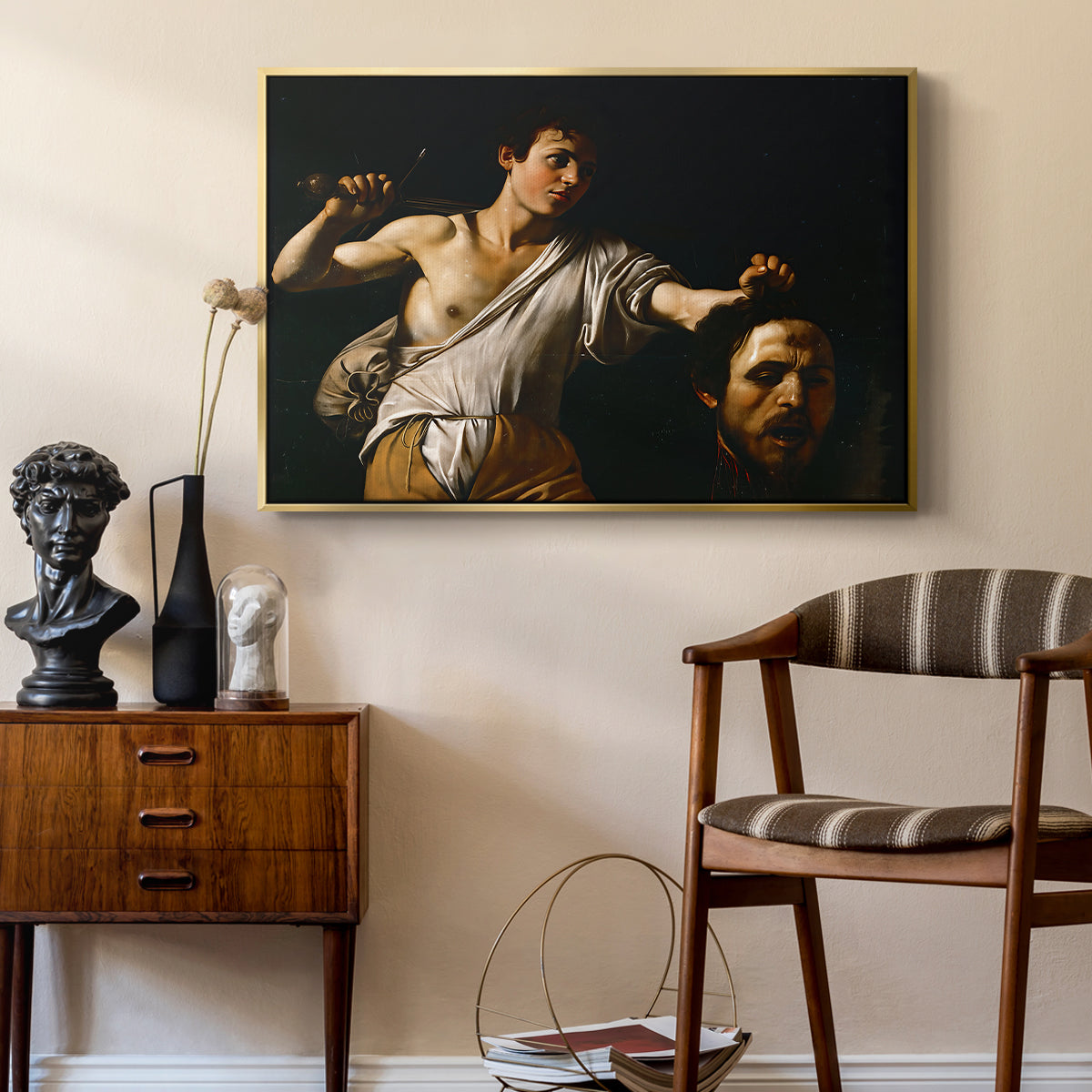 David with the Head of Goliath (Vienna Version), c. 1607 by Caravaggio as a gold floater framed canvas featuring a Baroque depiction of youth holding severed head in shadowy setting, styled above a mid-century console in a contemporary living area.