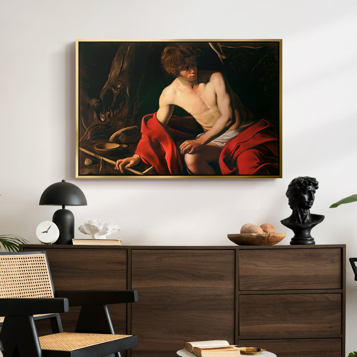 Saint John the Baptist in the Wilderness, c. 1603-1604 by Caravaggio displayed in a gold floater framed canvas above a dark wood credenza in an entryway.