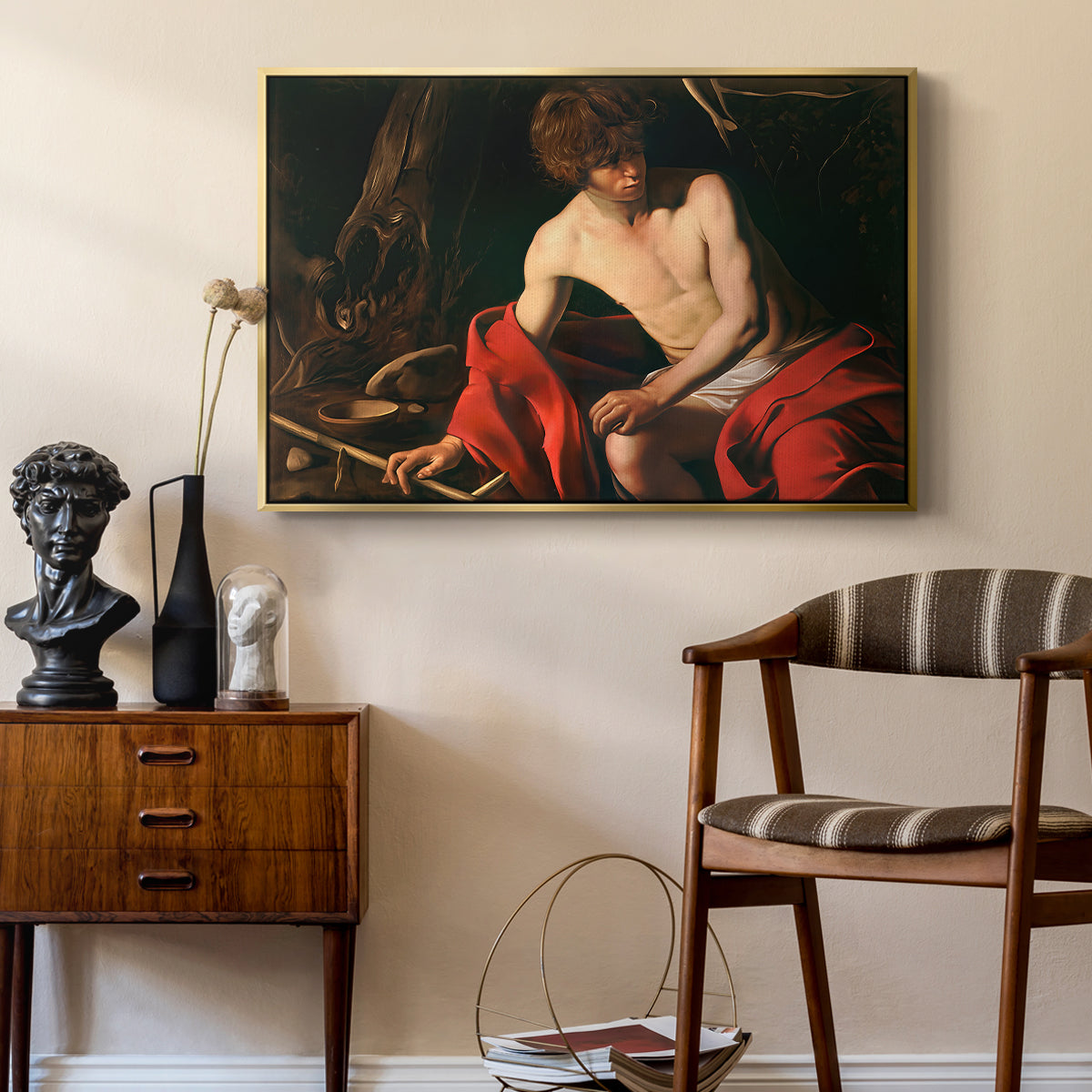 Saint John the Baptist in the Wilderness, c. 1603-1604 by Caravaggio as a gold floater framed canvas featuring a biblical youth seated outdoors with symbolic staff and minimal landscape, styled above a mid-century console in a contemporary living area.