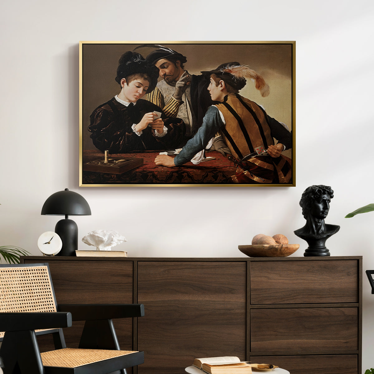 The Cardsharps, c. 1594 by Caravaggio displayed in a gold floater framed canvas above a dark wood credenza in an entryway.