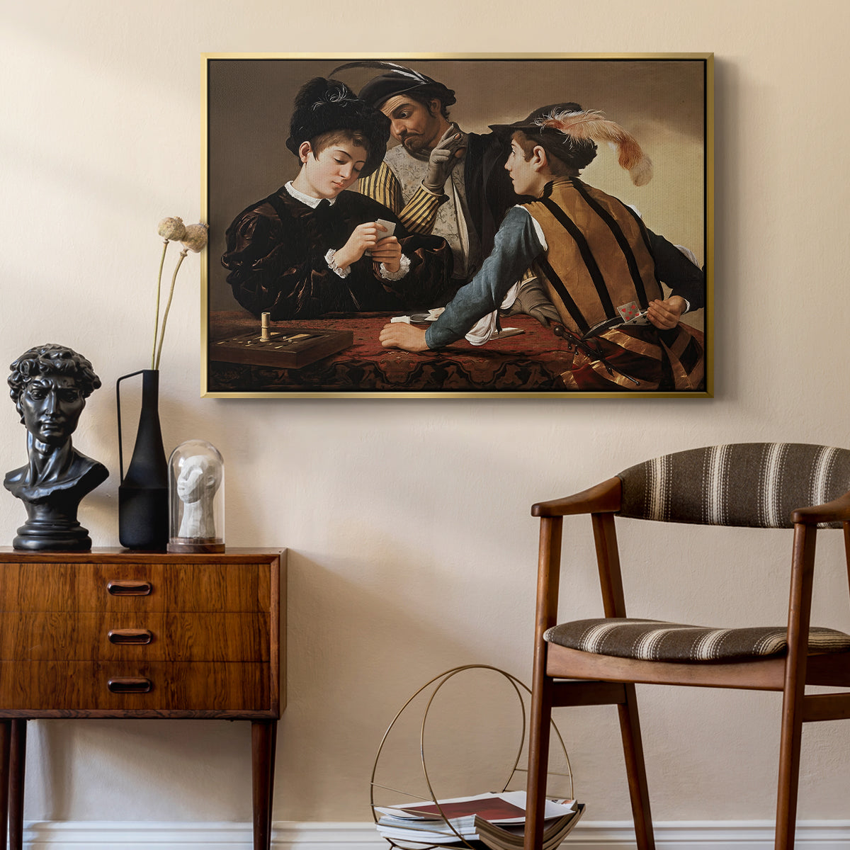 The Cardsharps, c. 1594 by Caravaggio as a gold floater framed canvas featuring a young men playing cards with one cheating and another watching closely, styled above a mid-century console in a contemporary living area.