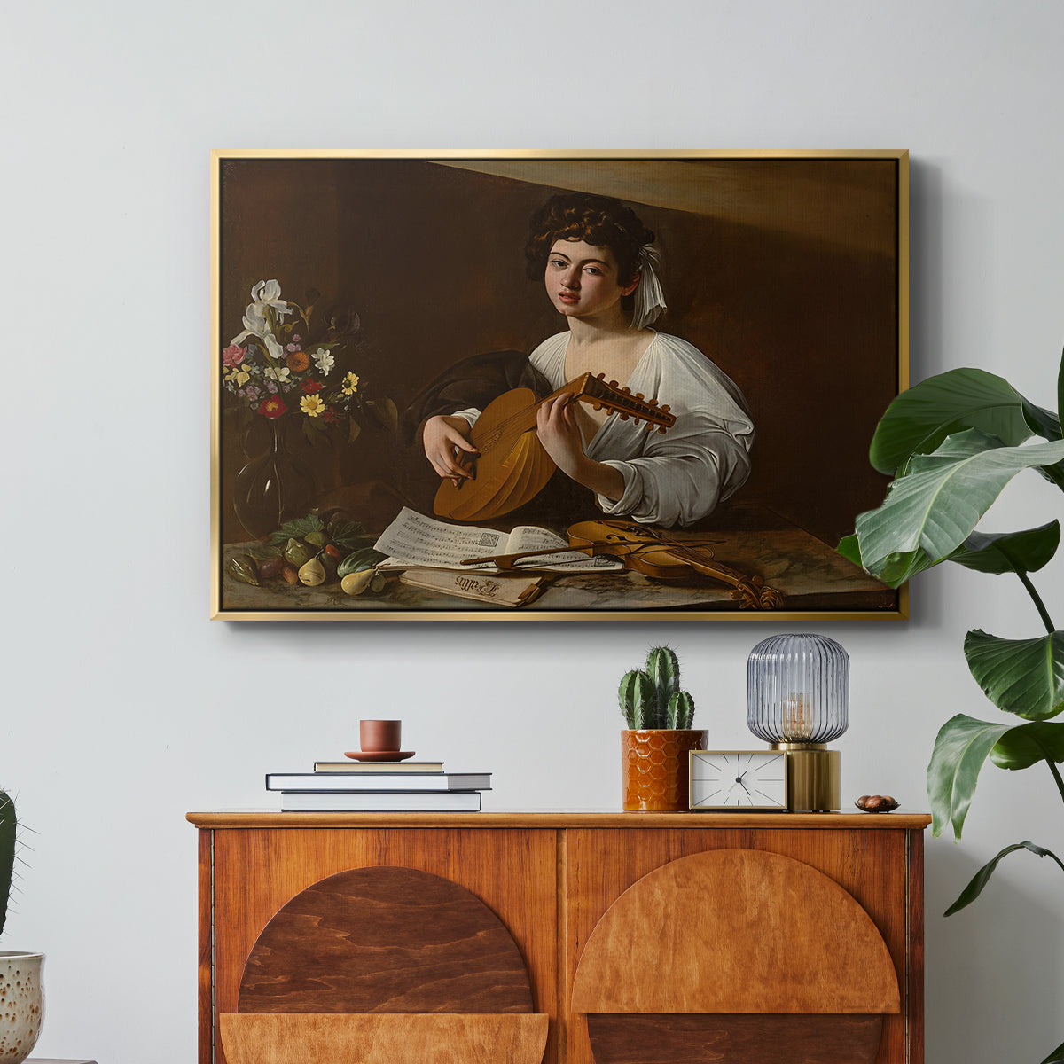 The Lute Player (Hermitage Version), c. 1596 by Caravaggio in a gold floater framed canvas featuring a young musician playing lute beside table with fruit and sheet music, displayed above a wood console cabinet.