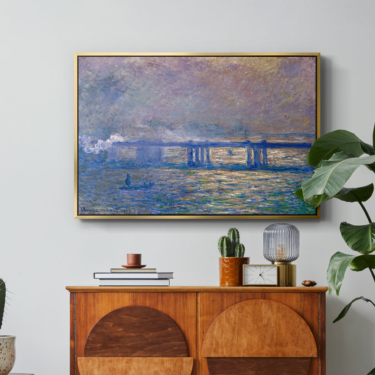 Charing Cross Bridge, 1903 by Claude Monet in a gold floater framed canvas featuring an impressionist view of bridge stretching across river with soft light and haze, displayed above a wood console cabinet.