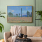 Gold floater framed canvas featuring a rural field filled with red blossoms beneath open sky, displayed above a sofa in a modern living room.