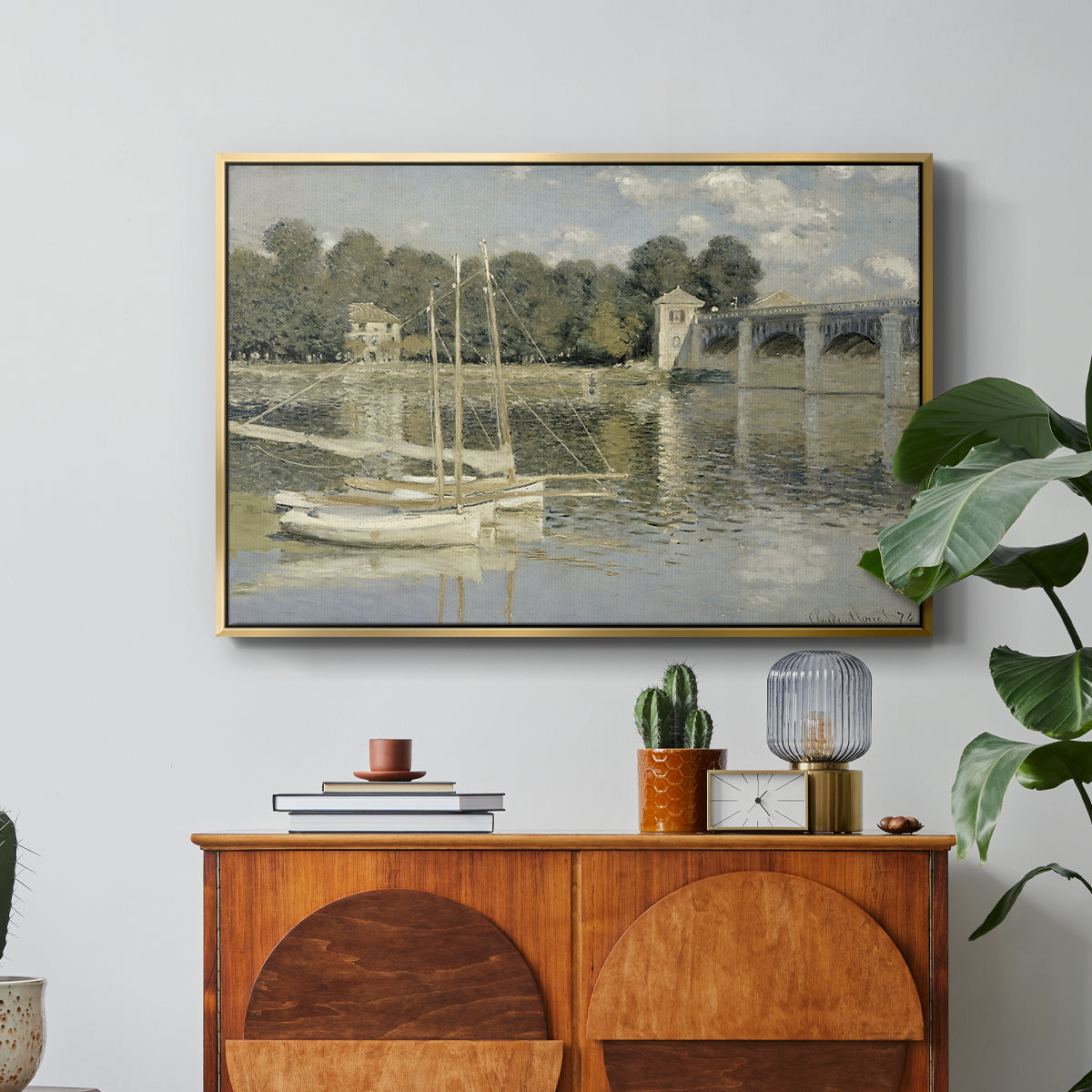 The Bridge at Argenteuil, 1874 by Claude Monet in a gold floater framed canvas featuring a bridge spanning river with sailboats and reflections in water, displayed above a wood console cabinet.