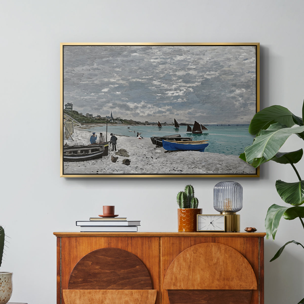 The Beach at Sainte-Adresse, 1867 by Claude Monet in a gold floater framed canvas featuring a seaside promenade with figures, flags, and boats along the coast, displayed above a wood console cabinet.