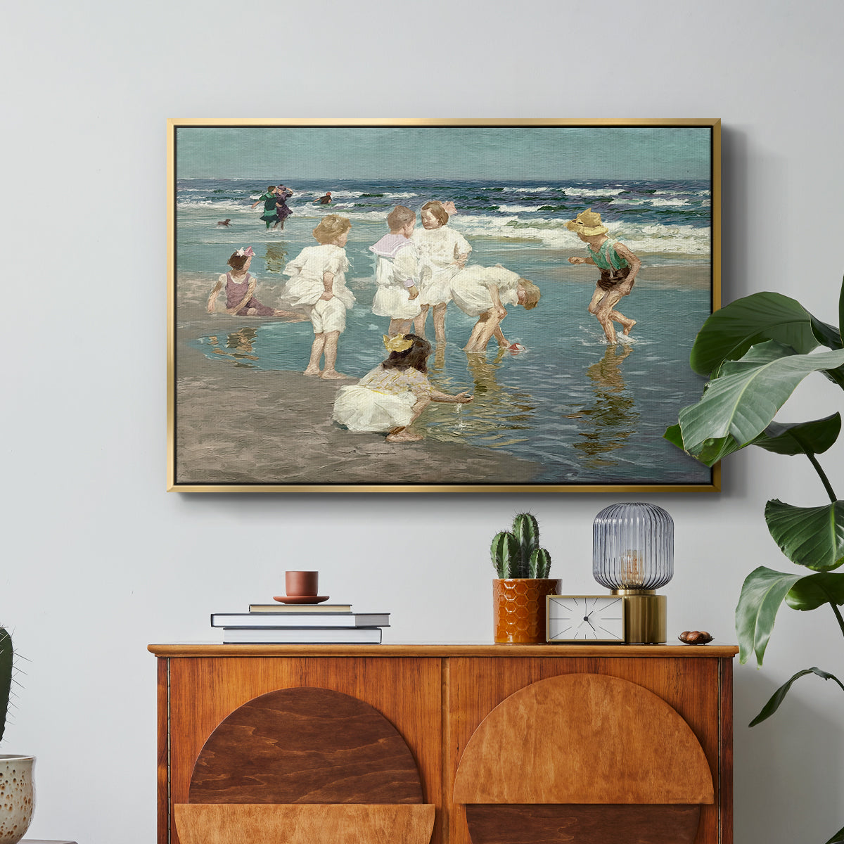 A Holiday, c. 1915 by Edward Henry Potthast in a gold floater framed canvas featuring people relaxing and wading in shallow ocean water along a sunny beach, displayed above a wood console cabinet.