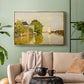Gold floater framed canvas featuring a peaceful village scene with houses bordering water, displayed above a sofa in a modern living room.