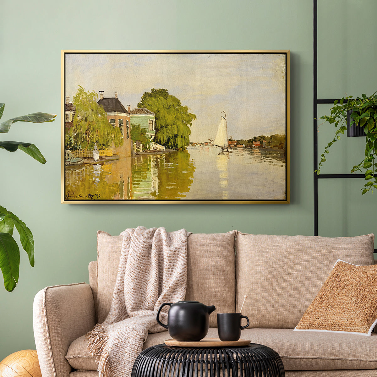 Gold floater framed canvas featuring a peaceful village scene with houses bordering water, displayed above a sofa in a modern living room.
