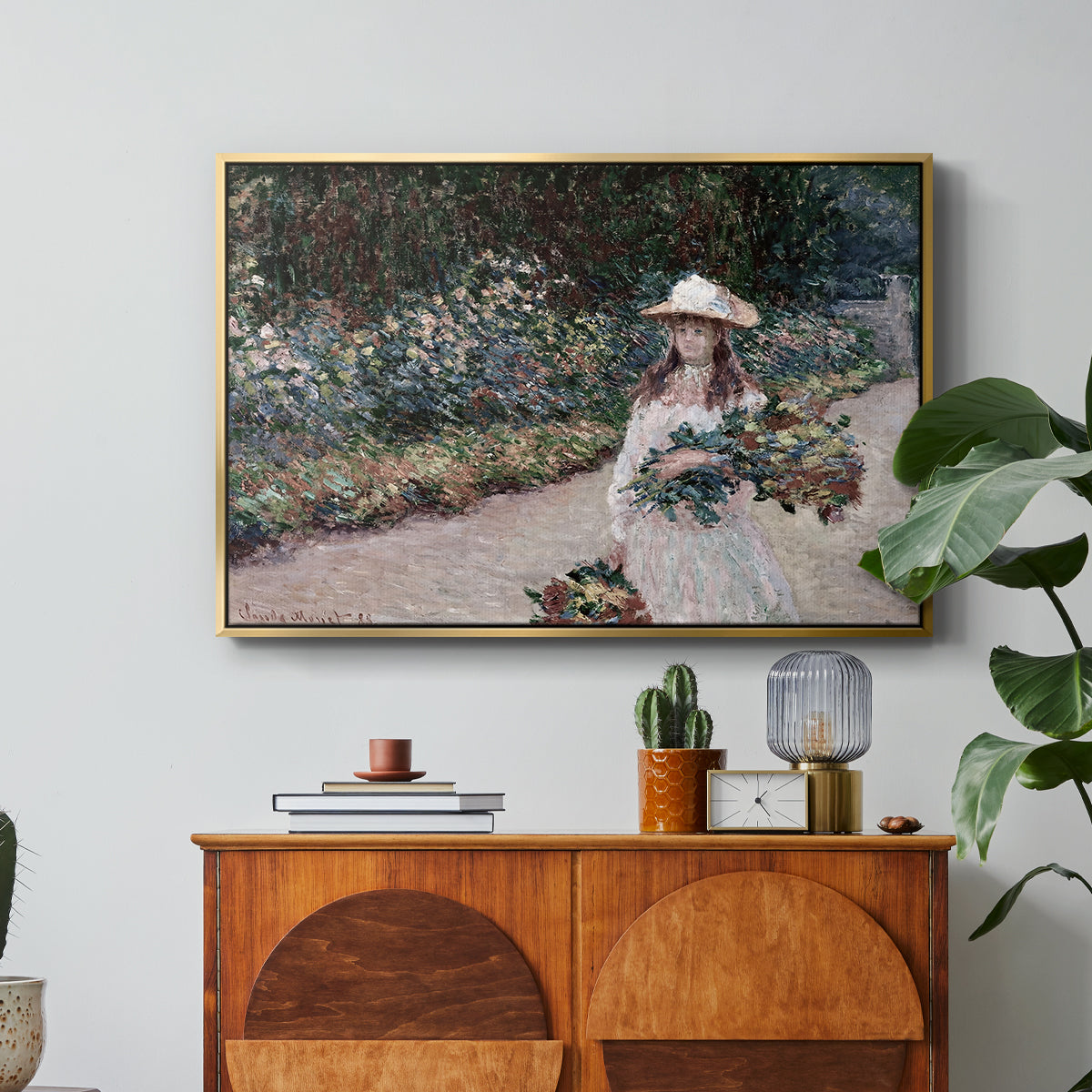Young Girl in the Garden at Giverny, 1888 by Claude Monet in a gold floater framed canvas featuring a young girl seated in lush garden surrounded by blooming flowers, displayed above a wood console cabinet.