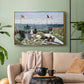 Gold floater framed canvas featuring a landscaped terrace with figures and flags near shoreline, displayed above a sofa in a modern living room.
