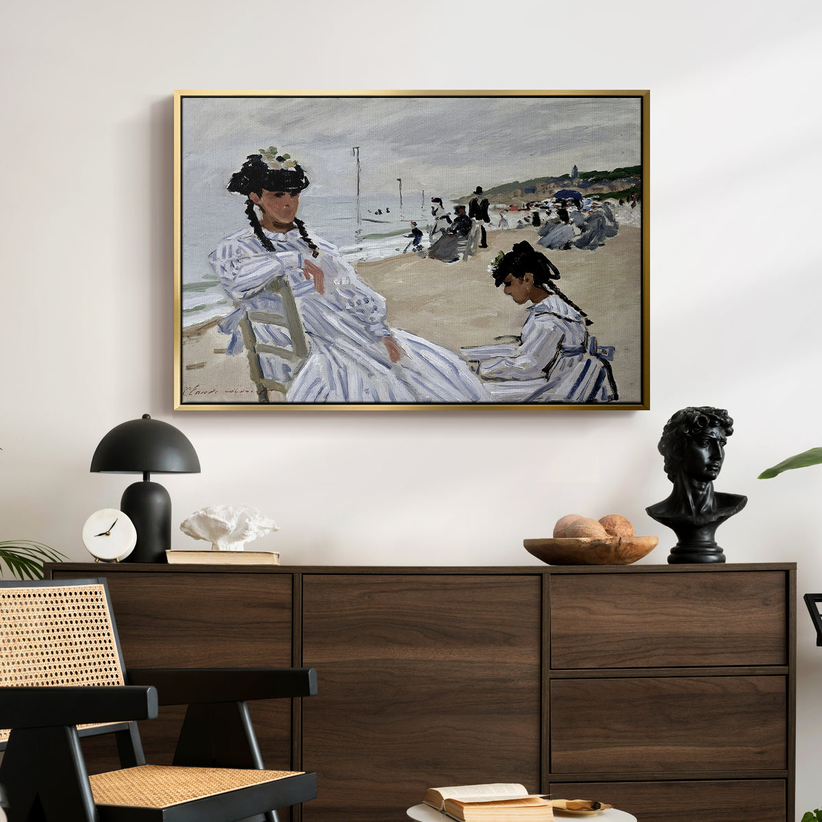On the Beach at Trouville, 1870 by Claude Monet displayed in a gold floater framed canvas above a dark wood credenza in an entryway.