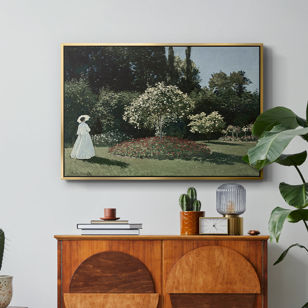 Woman in the Garden, Sainte-Adresse, 1867 by Claude Monet in a gold floater framed canvas featuring a woman standing in garden surrounded by flowers and greenery, displayed above a wood console cabinet.