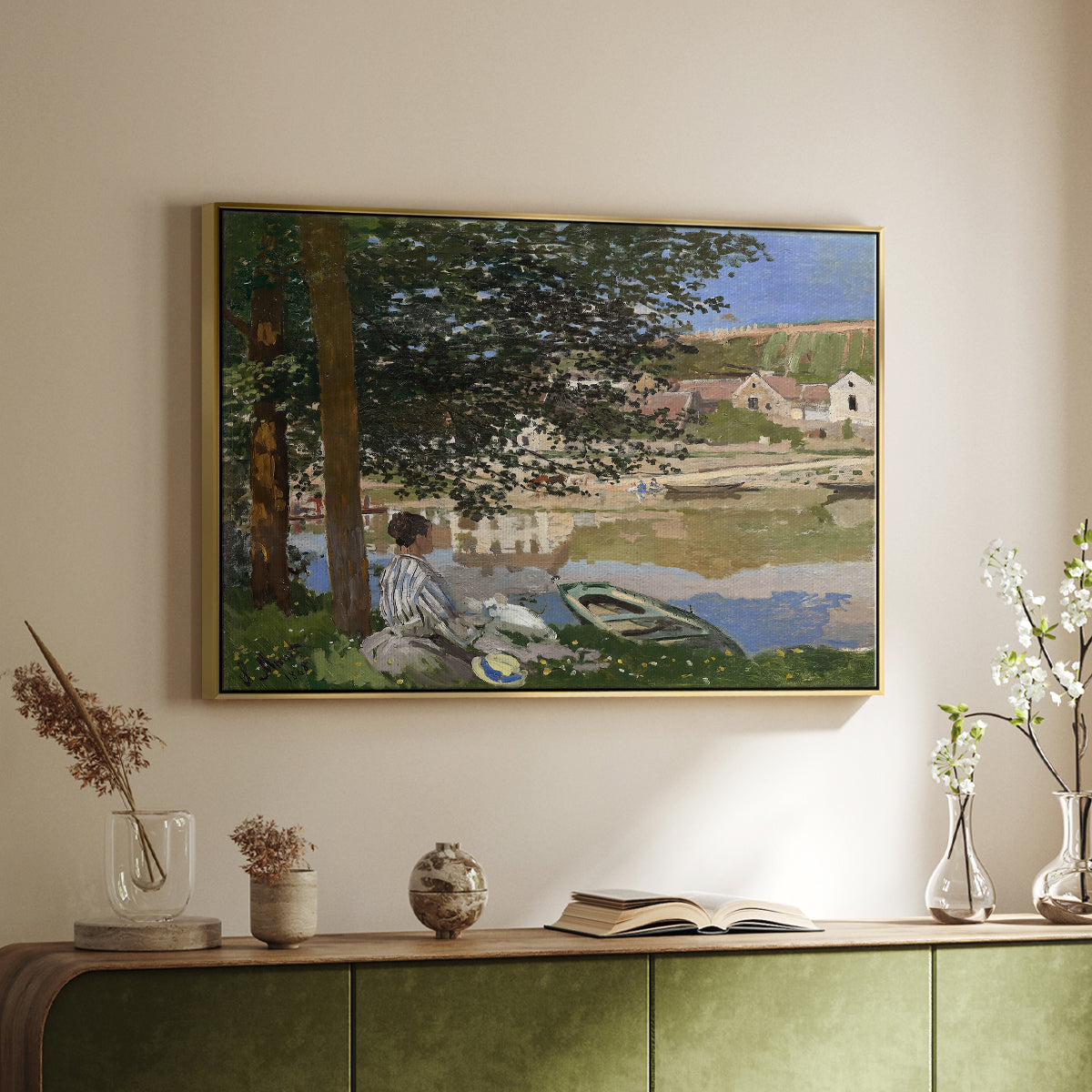 Gold floater framed canvas of On the Bank of the Seine, Bennecourt, 1868 by Claude Monet, featuring a peaceful riverside scene with figures resting in grassy area by water above a sideboard in a softly lit hallway.