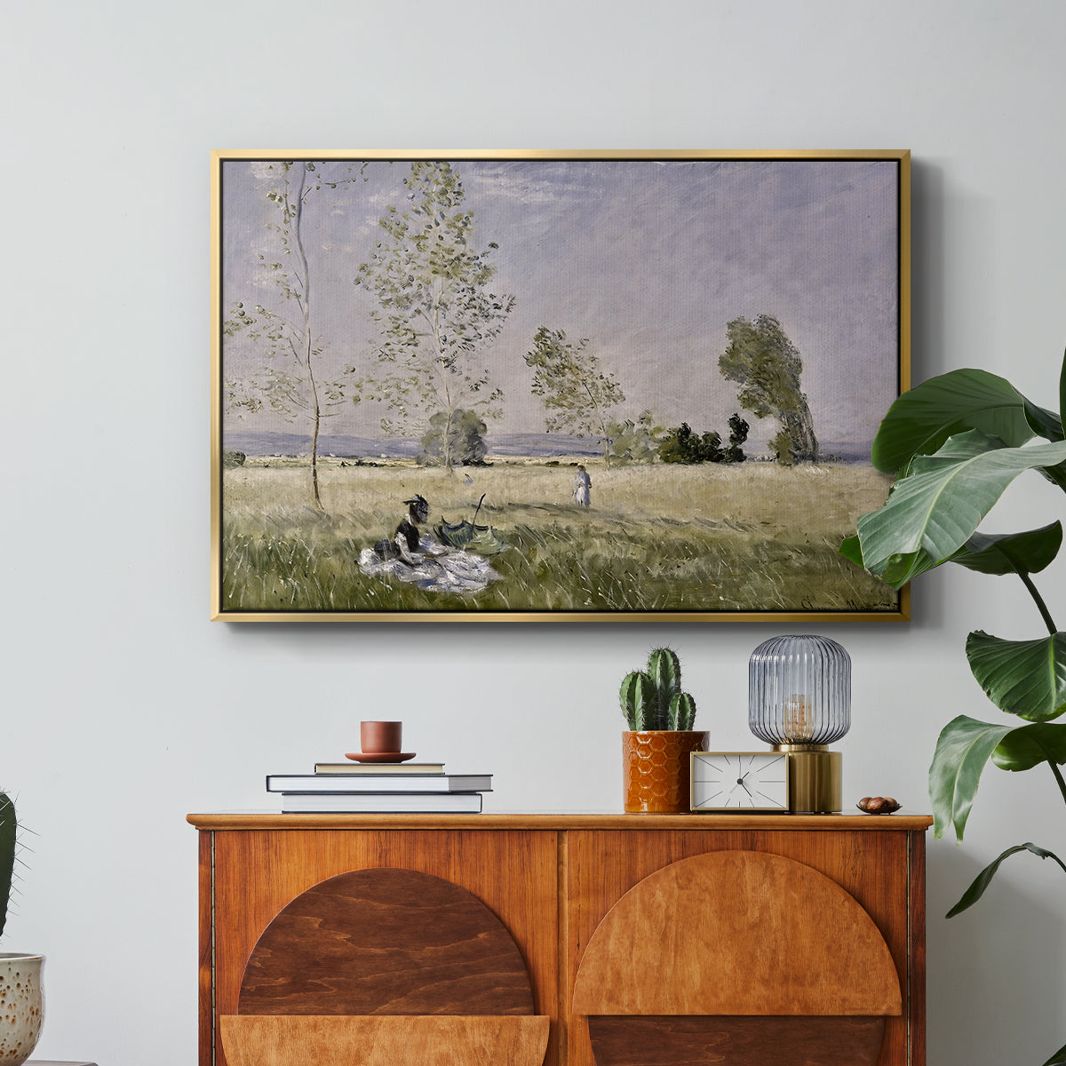 Summer (L'ete), 1874 by Claude Monet in a gold floater framed canvas featuring a woman seated in grassy field beneath tree in bright summer landscape, displayed above a wood console cabinet.