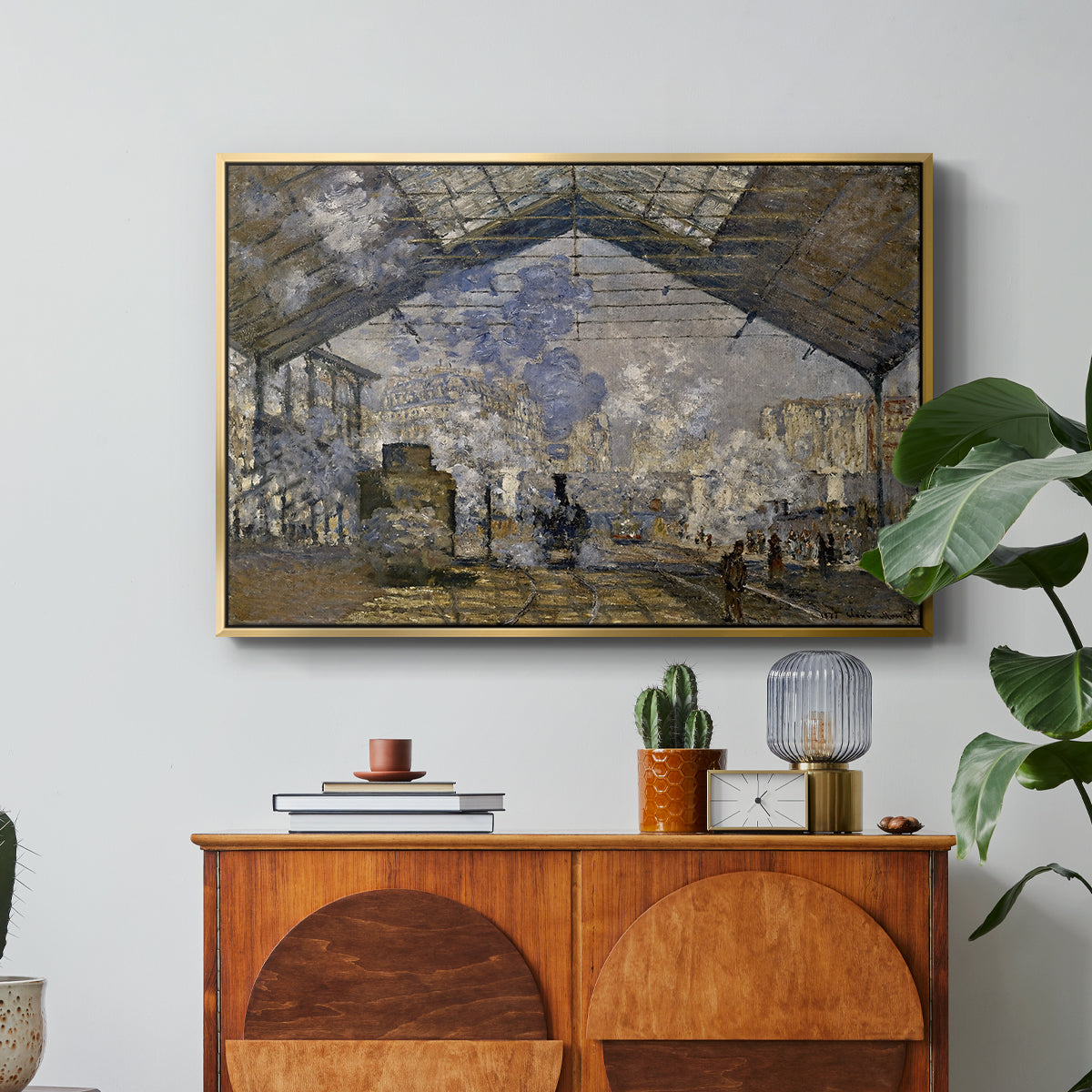 The Gare Saint-Lazare, 1877 by Claude Monet in a gold floater framed canvas featuring a train station interior filled with steam and locomotives under iron structure, displayed above a wood console cabinet.