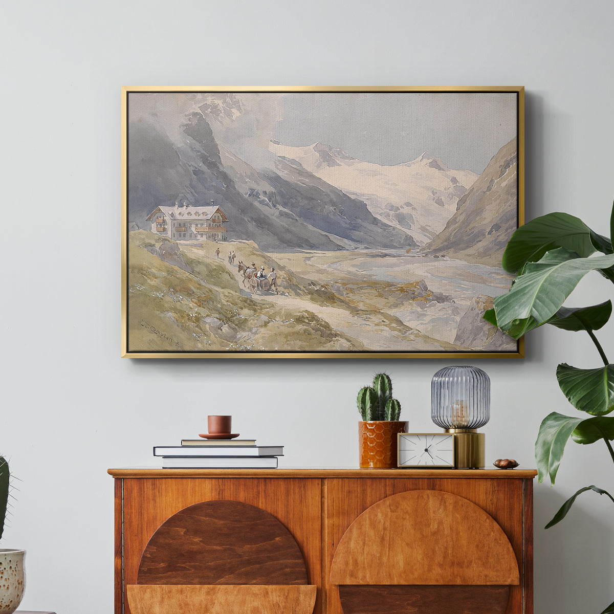 Shepherds (Pasterze), c. 1921 by Edward Theodore Compton in a gold floater framed canvas featuring a small group of shepherds in alpine landscape with grazing animals, displayed above a wood console cabinet.