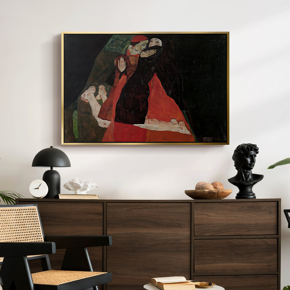 Cardinal and Nun (Caress), 1912 by Egon Schiele displayed in a gold floater framed canvas above a dark wood credenza in an entryway.
