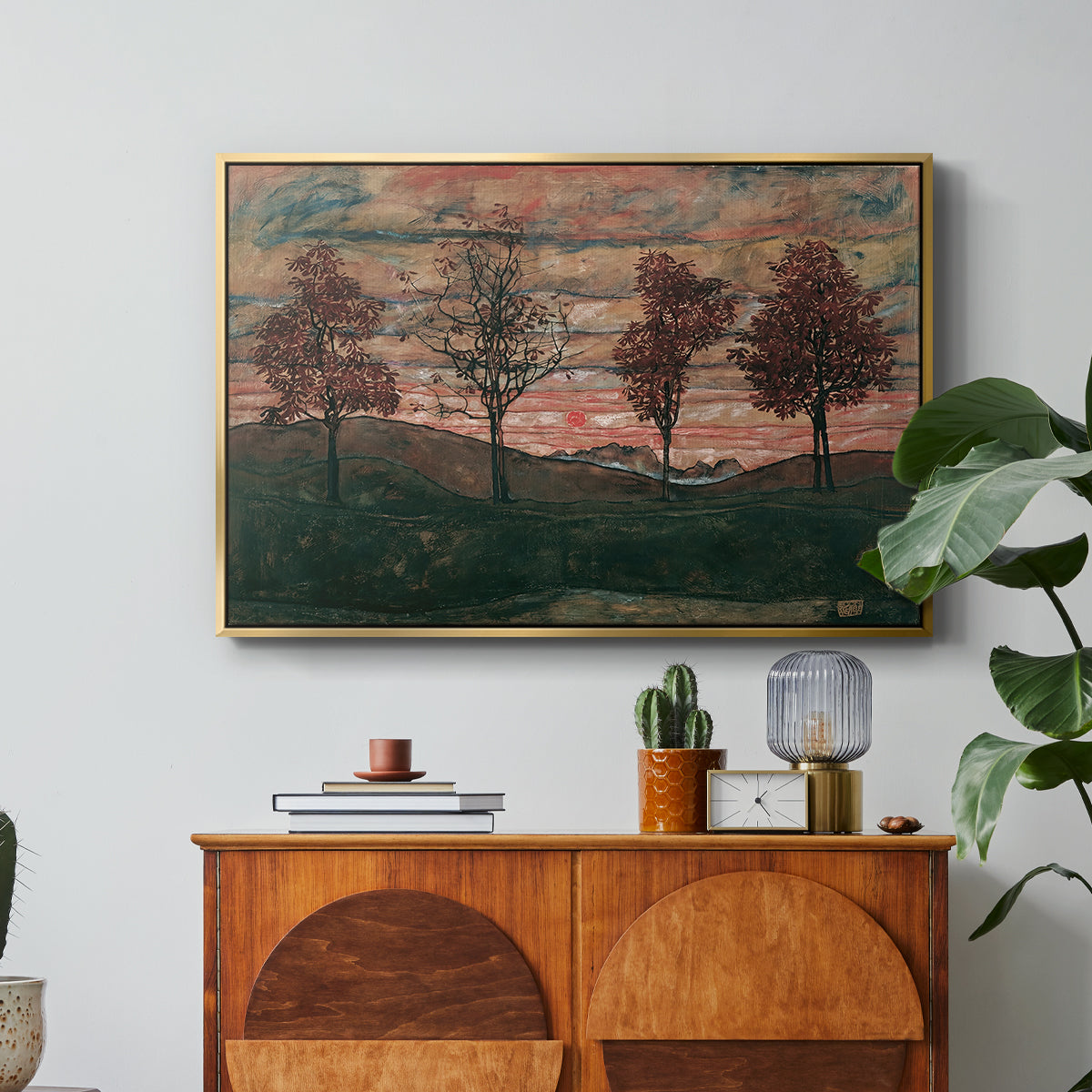 Four Trees, 1917 by Egon Schiele in a gold floater framed canvas featuring four trees standing in open landscape against colorful sky, displayed above a wood console cabinet.