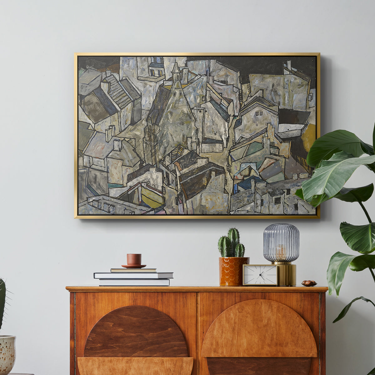 Mödling II, 1918 by Egon Schiele in a gold floater framed canvas featuring clustered geometric houses forming dense urban landscape with sharp angles, displayed above a wood console cabinet.