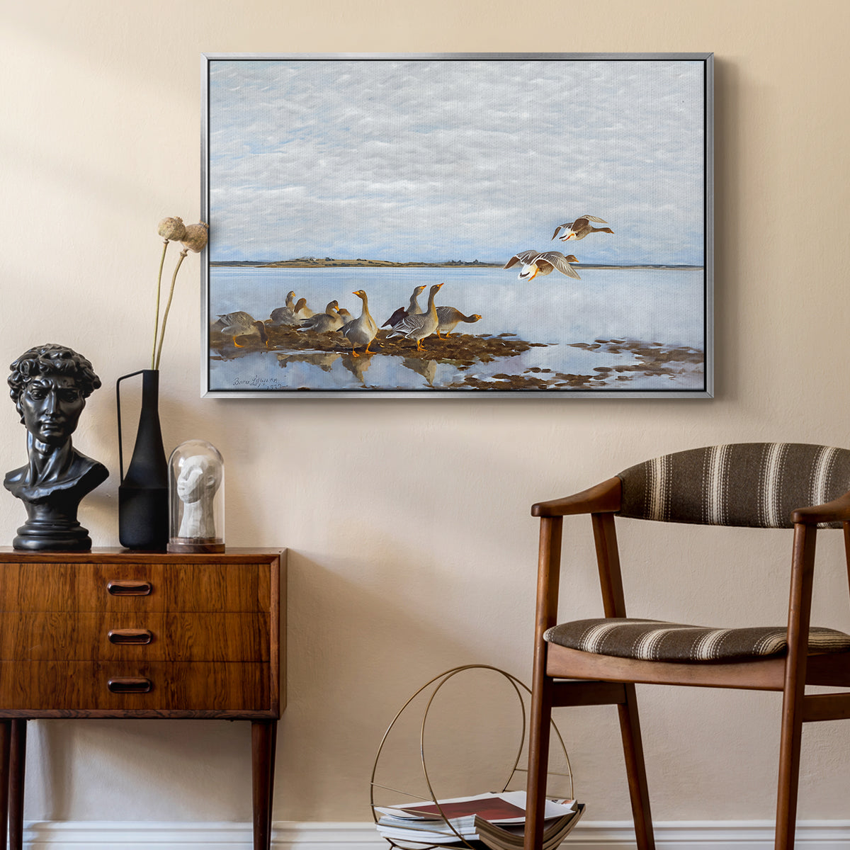 Greylag Geese (Grågäss), 1922 by Bruno Liljefors as a silver floater framed canvas featuring a realistic wildlife scene of geese in calm outdoor environment, styled above a mid-century console in a contemporary living area.